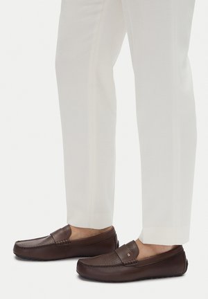 Brązowe skórzane mokasyny z perforowanym wzorem i gładkimi akcentami. Zestawione z białymi, dopasowanymi spodniami, tworząc elegancki, casualowy wygląd.