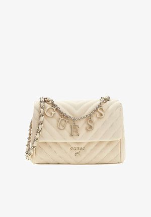 Sac à épaule matelassé beige avec bandoulière chaîne dorée et lettres suspendues formant "GUESS" au-dessus du logo de la marque sur le rabat avant.