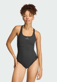 Čierne plavky s priliehavým dizajnom, sieťkovými akcentmi a širokými ramienkami so diskrétnym logom na hrudi. Hladký materiál a vysoké vykrojenie nohavíc.