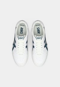 Valged spordijalatsid tumesiniste aktsentidega, millel on tekstureeritud pind, perforeeritud varvas, nööbid ja logo keelel.