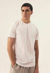 Biała koszulka z krótkim rękawem o okrągłym dekolcie, wykonana z gładkiego materiału, w zestawie z jasnoszarymi krótkimi spodniami z bocznymi kieszeniami.