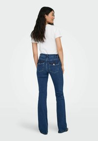 Ciemnoniebieskie dżinsy w kształcie dzwonów z wysokim stanem, z tylnymi kieszeniami i srebrnymi guzikami, zestawione z dopasowaną białą koszulką.