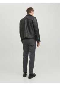 Giacca in pelle nera con un design leggermente corto, abbinata a pantaloni grigi. Presenta una trama liscia e accenti hardware minimalisti.