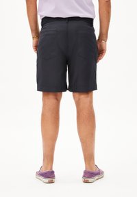 Shorts en coton navy avec une coupe droite, dotés de deux poches arrière et d'une ceinture épurée. Portés avec des chaussures en toile violettes.