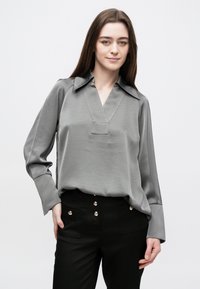 Γκρι σατέν μπλούζα με V-λαιμόκοψη και φαρδιά γιακά, μακριά μανίκια και διακριτική λάμψη, σε συνδυασμό με ψηλόμεσο μαύρο παντελόνι με λαμπερά κουμπιά.