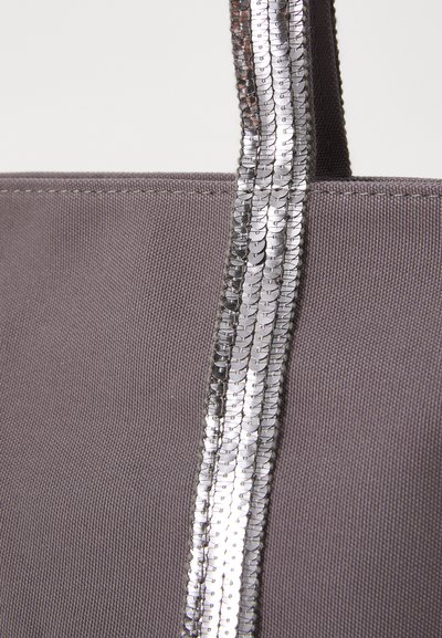 Gray fabric tote bag featuring a sequined silver stripe along the handle, highlighting its texture and design details.