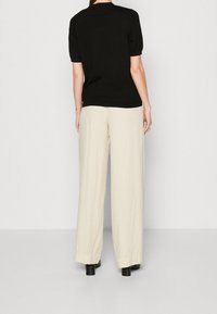 Černé tričko s krátkým rukávem spárované s krémovými volnými kalhotami. Kalhoty mají hladkou texturu a diskrétní detaily na lemech, které dokončují vzhled outfitu.