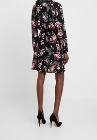 Černé květinové šaty s dlouhými rukávy, stahovaným pasem a rozšířenou sukní. Mají barevný vzor květin na tmavém pozadí.