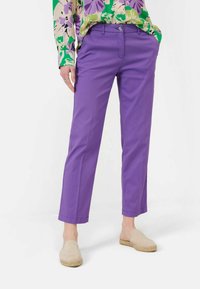 Pantalon en coton violet à coupe droite, avec poches latérales et ourlets cousus, associé à des chaussures légères beiges à enfiler.