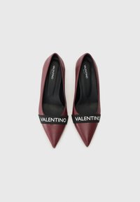 Scarpe in pelle borgogna con punta affusolata, dotate di una fascia nera con "VALENTINO" in testo bianco sulla parte superiore.