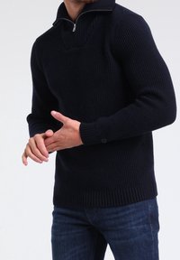 Pull côtelé bleu marine avec un col montant et une fermeture à glissière mi-longue. Dispose de manches longues et d'une coupe ajustée avec ourlet et poignets côtelés.