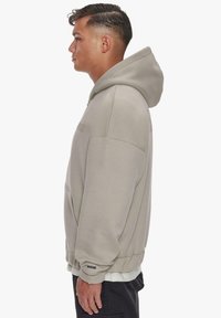 Light grey hoodie with a front pocket, hood, and ribbed cuffs. Soft fabric and relaxed fit, featuring a subtle brand logo on the chest.
