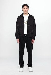 Schwarze Bomberjacke mit kontrastierenden weißen Nähten, kombiniert mit einem weißen T-Shirt mit Grafik und schwarzen Hosen, abgerundet mit weißen Sneakers.