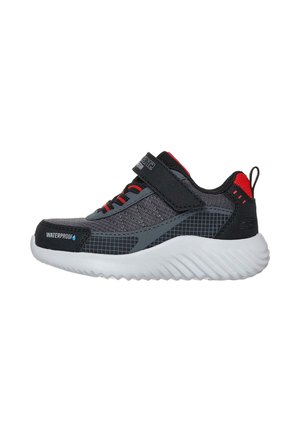 Zapatilla impermeable para niños en negro y gris con detalles rojos, cierre de velcro y suela blanca gruesa, vista lateral.