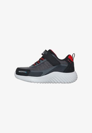 Zapatilla impermeable para niños en negro y gris con detalles rojos, cierre de velcro y suela blanca gruesa, vista lateral.