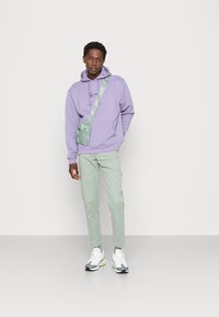 Lavender hoodie with front logo, light green cargo pants, and gray sneakers with yellow accents. Includes a small mint crossbody bag.