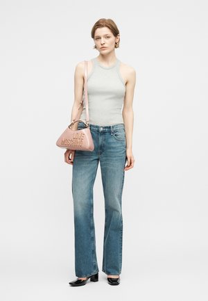 Kvinde iført grå ærmeløs top, blå jeans, sorte hæle og bærende en lyserød "LOVE MOSCHINO" skuldertaske.