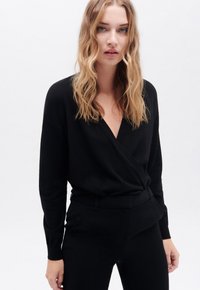 Zwarte wikkelstijl pullover gemaakt van zachte stof, met lange mouwen en een V-hals. Gedeeltelijk gedragen met bijpassende zwarte taillepants. Minimalistisch ontwerp.