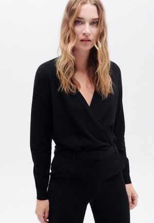Zwarte wikkelstijl pullover gemaakt van zachte stof, met lange mouwen en een V-hals. Gedeeltelijk gedragen met bijpassende zwarte taillepants. Minimalistisch ontwerp.
