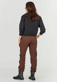 Felpa nera con polsini a coste, pantaloni cargo marroni con texture stropicciata e stivaletti neri stringati alla caviglia. Vista posteriore.