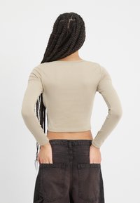 Beige hosszú ujjú crop top, testhezálló fazonnal. Simogató tapintású anyag és kerek nyakkivágás. Sötét cargo nadrággal viselve, kezek a zsebekben.