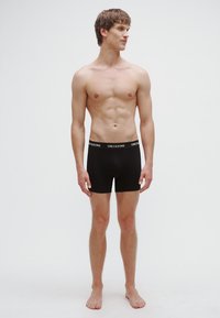 Black boxer briefs with a logo waistband, made of smooth fabric. Designed for a snug fit, featuring a straight leg cut and minimalist style.