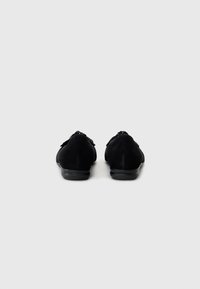 Schwarze Wildlederschuhe mit runder Zehenpartie und niedrigem Absatz. Die Rückansicht zeigt ein minimalistisches Design ohne sichtbare Muster oder Metallakzente.
