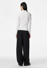 Bílý top s dlouhým rukávem s žebrovanou strukturou, doplněný černými kalhotami s širokými nohavicemi, zobrazený zezadu na jednobarevném pozadí.