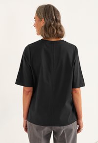 Mustapaitainen lyhythihainen paita, jossa on pyöreä pääntie ja pystysaumadetaljointi selässä, valmistettu sileästä ja kevyestä kankaasta.