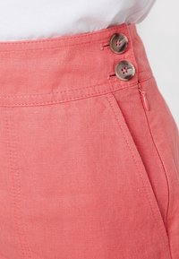 Vaaleanpunaiset pellavahousut, joissa on korkea vyötärö, kaksi ruskeaa nappia ja sivuzipperi. Rakenne, jossa on puhdas sauman viimeistely.