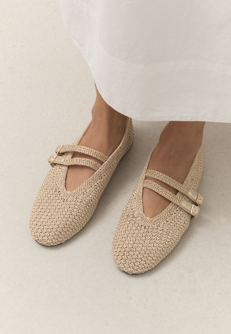Pieds portant des ballerines tissées beiges avec des brides à double boucle, associées à une jupe longue ou une robe de couleur claire.
