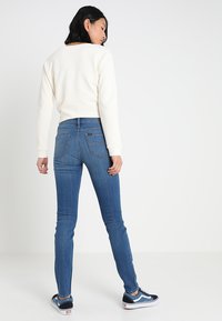Vit kortärmad sweatshirt, blå skinny jeans och svarta sneakers. Slät textur, åtsittande silhuett, med klassiska bakfickor på jeansen.