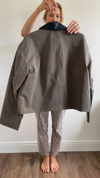 Jachetă gri cu guler negru, având o croială lejeră și un design minimalist. Materialul pare neted; prezentată de o persoană.
