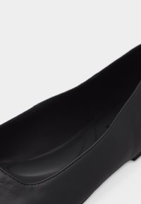 Γυναικείο μαύρο δερμάτινο παπούτσι φλατ με στρογγυλεμένη μύτη και χαμηλό τακούνι, εμφανιζόμενο από κοντινή πλευρική γωνιακή θέα.