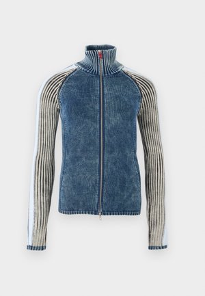 Jachetă tricotată albastră cu fermoar, guler înalt și mâneci lungi cu dungi verticale albe și negre.