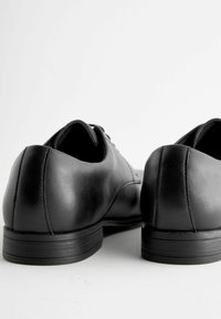 Czarne skórzane buty o gładkiej fakturze, zaokrąglonym obcasie i subtelnych detalach przeszycia. Projekt cechuje klasyczny styl na sznurówki.