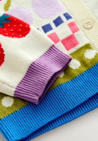 Close-up of colorful knit sweaters featuring a purple cuff, strawberry pattern, blue ribbed hem, polka dots, and geometric shapes with buttons.