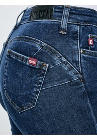 Suur lähedalt tumesinise teksapükste tagatasku, kus on punane Big Stari kaubamärgiga silt ja must märk vöökohal.