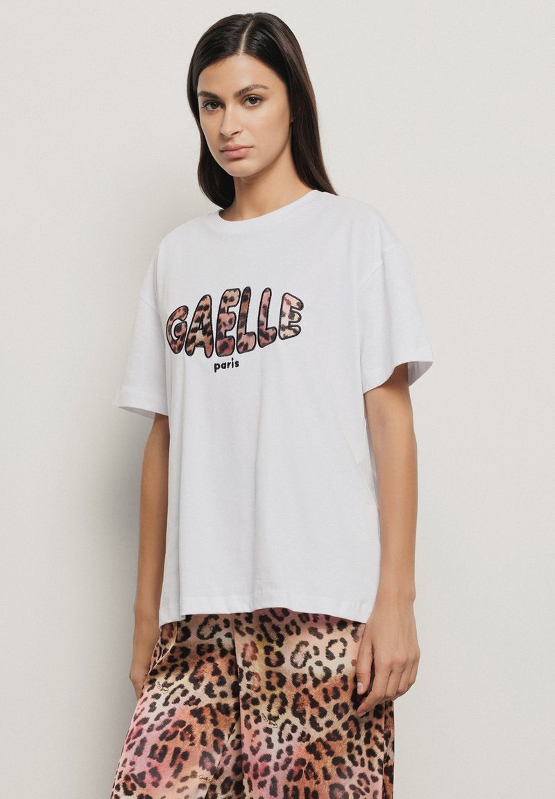 T-shirt in cotone bianco con stampa in grassetto "GAELLE paris" in lettere con stampa animale testurizzata. Vestibilità ampia con scollo rotondo e maniche corte.