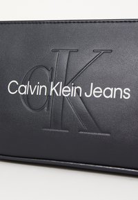 Fekete bőr pénztárca dombornyomott "CK" logóval és fehér betűkkel kiírt "Calvin Klein Jeans" felirattal. Simább textúra és letisztult dizájn.