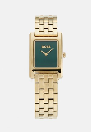 Montre rectangulaire dorée avec un cadran vert, portant le nom de la marque "BOSS" et un bracelet en maillons métalliques. Aiguilles épurées et détail de couronne.