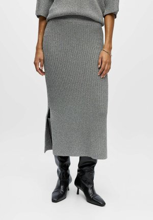 Grau gestrickter Rock mit gerippter Textur, knielang und mit seitlichem Schlitz, kombiniert mit schwarzen spitzen Stiefeletten. Der Pullover hat ein ähnliches Design.