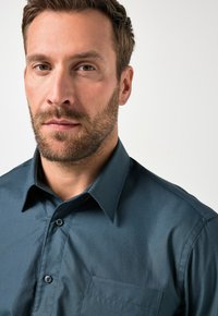 Ciemnoniebieska koszula z guzikami posiadająca standardowy kołnierzyk, jedną kieszeń na piersi oraz gładki, teksturowany materiał.