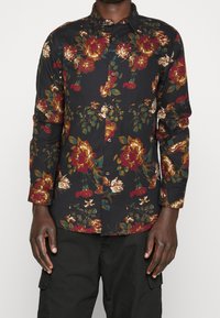 Svart långärmad skjorta med blommönster i röd, guld och grön. Har en knappstängning fram och en klassisk krage.