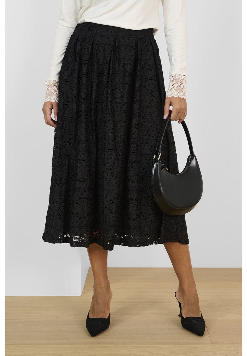 Zwarte kanten rok met een ingewikkeld bloempatroon, middellange lengte, geplooid ontwerp, gecombineerd met een zwarte ronde handtas en spitse zwarte hakken.