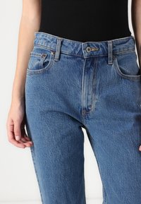 Blue denim jeans with a high waist, featuring a button closure, front pockets, and visible stitching. The fabric has a slightly worn texture.