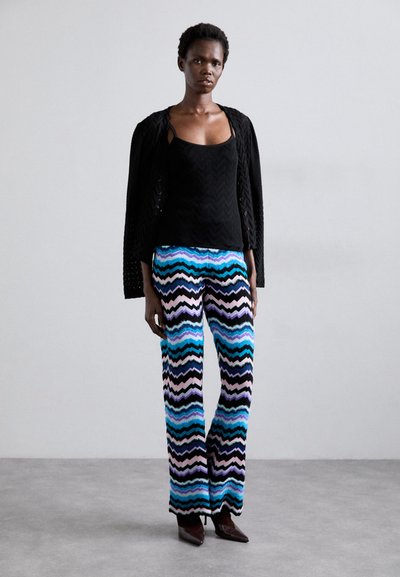 Black knitted top with textured pattern, paired with multicolored zigzag patterned wide-leg pants in blue, pink, and black shades. Brown heels.