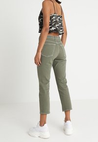 Top crop camouflage, jeans a vita alta verde oliva e sneakers bianchi. I jeans hanno due tasche posteriori e dettagli di cucitura sottili.