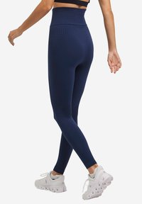 Marineblauwe high-waisted leggings met een gestructureerd patroon en een geribbelde tailleband, gecombineerd met witte sportschoenen.