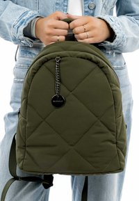 Mochila acolchada verde oliva con forma redondeada, cierre de cremallera, acento de cadena y tirantes ajustables; hecha de un material suave y texturizado.